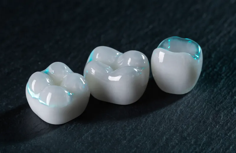 Three zirconia dental crowns photographed on dark slate